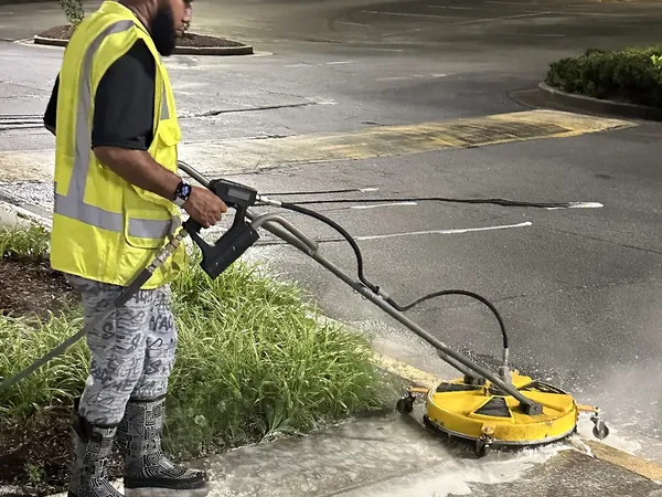 Georgia Bubbles crew member in a safety vest running a surface cleaner along the curb at a shopping center in Duluth at night