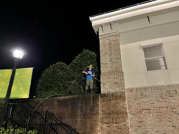 Georgia Bubbles technician pressure washing a brick facade at a shopping center at night